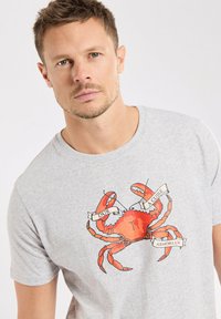 T-shirt en coton gris avec un grand graphique de crabe rouge accompagné de bannières inscrites "DUR" et "À CUIRE". Design classique à col rond.