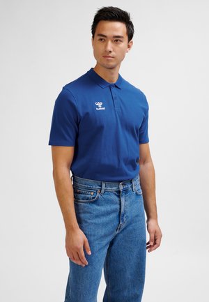 Blå polo skjorte med krave og korte ærmer, med en logo på venstre bryst. Kombineret med lyseblå denimjeans.