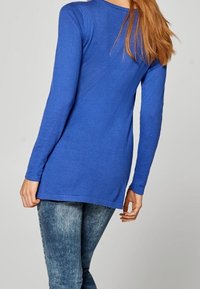 Modrý svetr s dlouhým rukávem a kulatým výstřihem, jemná textura a rovný střih. Nosený přes světle modré džíny.