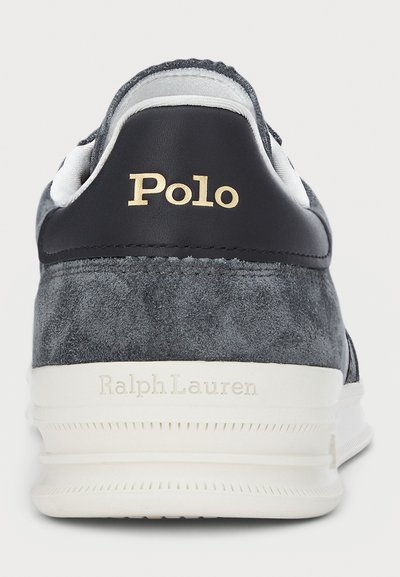 Grå mockaskor med vita accenter, med en marinblå läderklack och guld "Polo"-logotyp. Gummisula med texturerade detaljer.