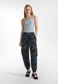 Lyseblå ribstrikket tanktop kombineret med sorte cargobukser med blomstermønster, med rynkede ærmekanter og sidelommer. Sorte sko fuldender looket.