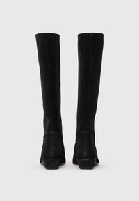 Botas altas de ante negras con un acabado texturizado, parte superior ligeramente ajustada y un tacón bajo y apilado. Diseño simple sin herrajes visibles.