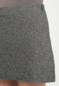 Mini-jupe grise à motif pied-de-poule en tissu texturé avec une fermeture éclair dissimulée sur le côté. Coupe ajustée avec une ligne droite.