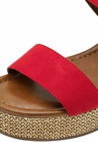 Sandale en tissu rouge avec une large sangle, semelle en cuir synthétique marron et semelle plateforme tressée ressemblant à du jute. Des détails texturés améliorent l'adhérence.