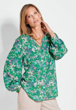 Blusa floreale verde con maniche lunghe e gonfie, chiusura a bottoni e scollo a V. Presenta una combinazione di motivi floreali in viola, blu e rosa.