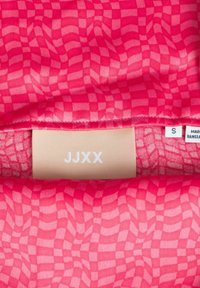 Różowa tkanina z wzorem w falistą kratę. Metka pokazuje rozmiar 'S' i markę 'JJXX' w białym kolorze. Miękka tekstura, typowa dla odzieży.