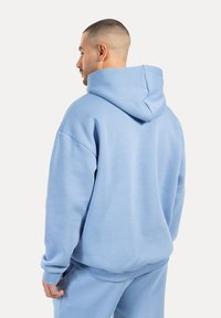 Sudadera oversize de color azul claro con una textura suave, capucha grande y puños y dobladillo acanalados, combinada con pantalones de chándal a juego.