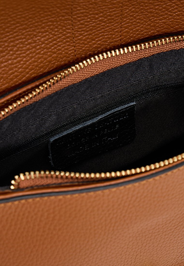 Intérieur d'un sac à main en cuir tan avec une doublure en tissu noir ; fermeture éclair dorée visible et étiquette en relief indiquant un savoir-faire italien.