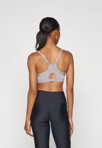 Gray sports bra with a cutout detail at the back and adjustable straps. Paired with high-waisted black leggings, featuring a smooth texture.