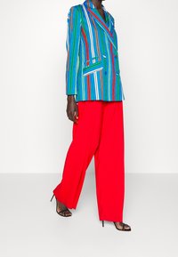 Gestreepte blazer in blauw, groen, rood en bruin met een dubbelreeks ontwerp, gecombineerd met brede rode broek en zwarte sandalen met bandjes.