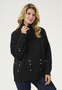 Svart stickad polotröja med lös passform. Inkluderar pärl-accenter och texturerade diamantmönster på den nedre delen. Ribbstickade ärmslut och nederkant.