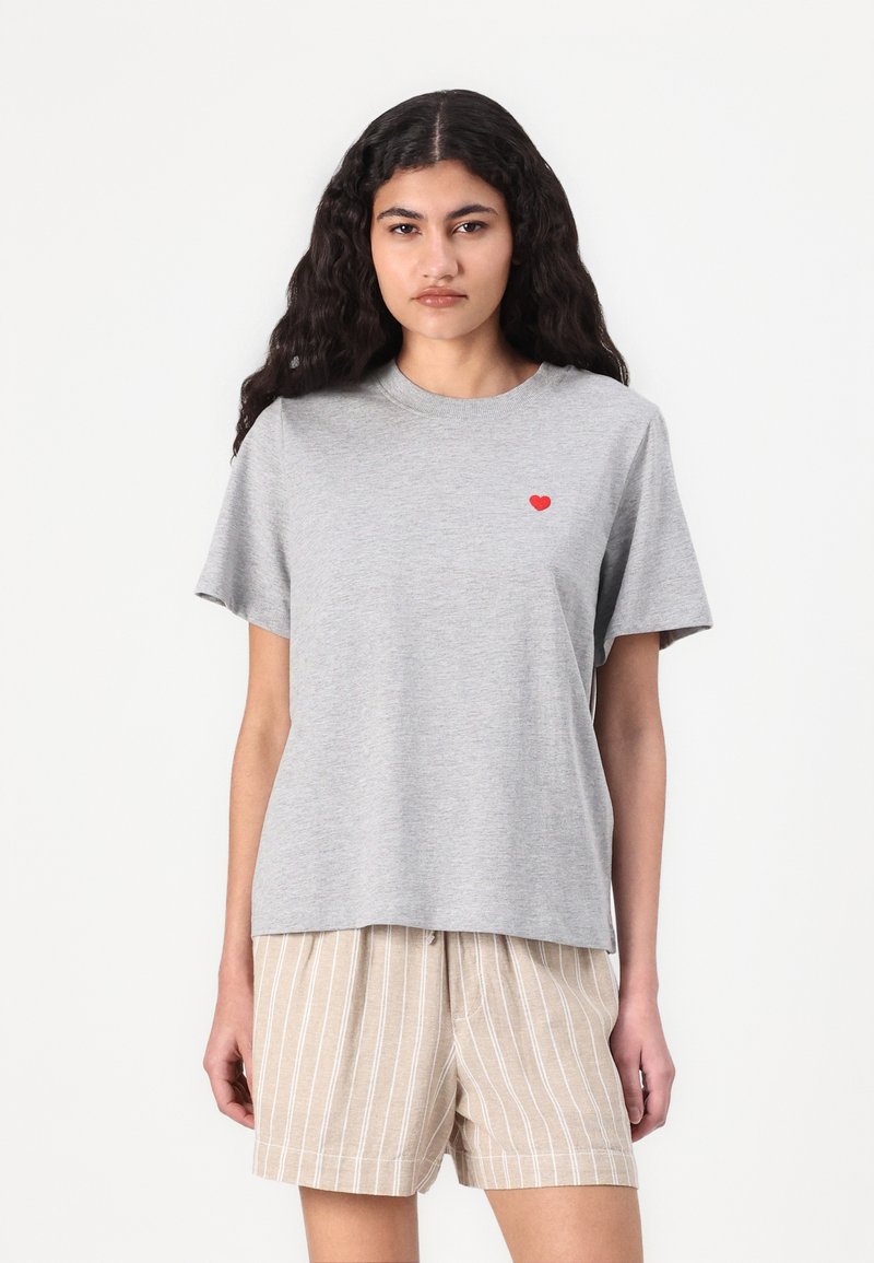 Gray cotton t-shirt with short sleeves, featuring a small red heart design on the left chest area. Worn with beige striped shorts.