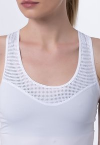 Débardeur athlétique blanc avec une partie supérieure en maille ajourée et un col rond. Tissu lisse et léger avec une coupe ajustée.