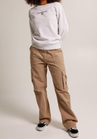 Sudadera gris claro con el texto "ESTADO DE NUEVA YORK", combinada con pantalones cargo beige que tienen bolsillos laterales y zapatillas negras.