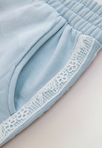 Material albastru deschis cu o talie elastică și marginea buzunarului decorată cu dantelă florală albă.