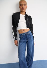 Veste noire courte avec rayures blanches, haut ajusté blanc et jeans bleu large taille haute. Design minimaliste avec accents métalliques.