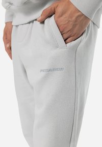 Pantalones de chándal gris claro con bolsillos laterales, cinturilla acanalada y un sutil texto de marca "PEGADOR" en el muslo. Material suave de mezcla de algodón.