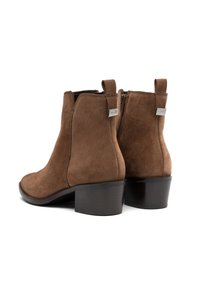 Bruna mockaskinn ankle boots med blockklackar, sidodragkedjor och dragflikar med varumärkeslapp på vit bakgrund.