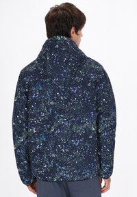 Marine blauwe pufferjas met een multikleurig spetterpatroon. Heeft een capuchon en elastische manchetten. Het materiaal lijkt glad en licht glanzend.