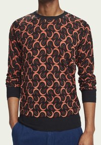 Pullover in un elegante colore nero con un motivo a spirale rosso e arancione. Caratterizzato da un collo a barchetta, maniche lunghe e polsini e orlo a coste.