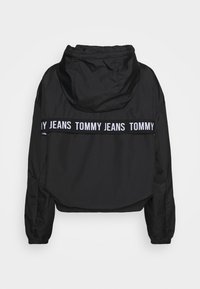 Zwarte hooded jack van lichtgewicht materiaal, met een cropped ontwerp, elastische manchetten en een contrasterende witte logoband op de rug.