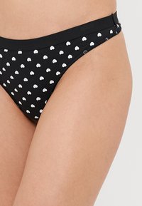 Musthave lille musta ujumispükse valgete südame mustritega, mis on siledate tekstuuride ja elastse vöökohaga mugavuseks.