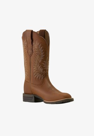 Botte de cowboy en cuir marron avec couture décorative, haut festonné, brides de traction, talon bas et semelle texturée.
