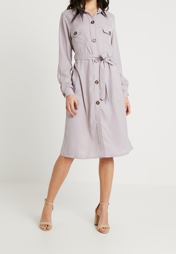 Robe chemise violet clair en tissu lisse, avec manches longues, boutonnage sur le devant, deux poches poitrine et une ceinture assortie à la taille.