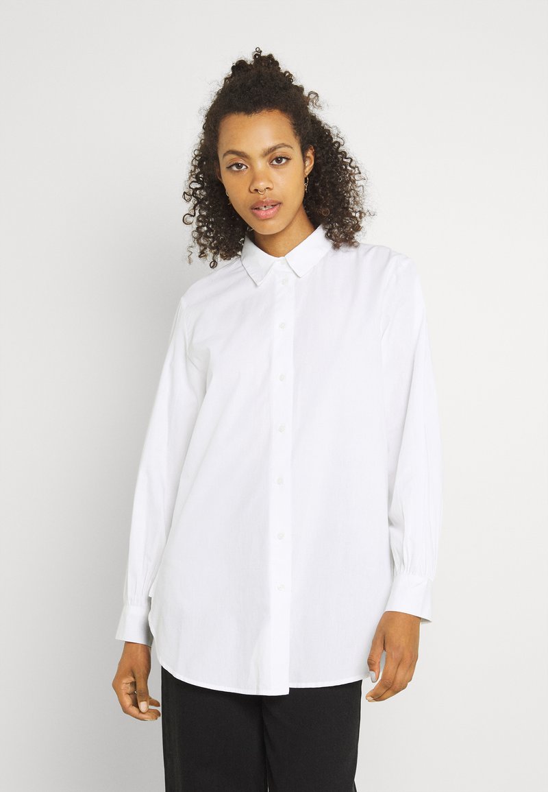 Camicia bianca a bottone con colletto, maniche lunghe e vestibilità rilassata. Realizzata in un tessuto liscio con una leggera texture. Caratteristiche di design classico.