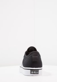 Black canvas sneaker with a white outsole, textured heel tab, and logo plate. Features stitched detailing and round laces.