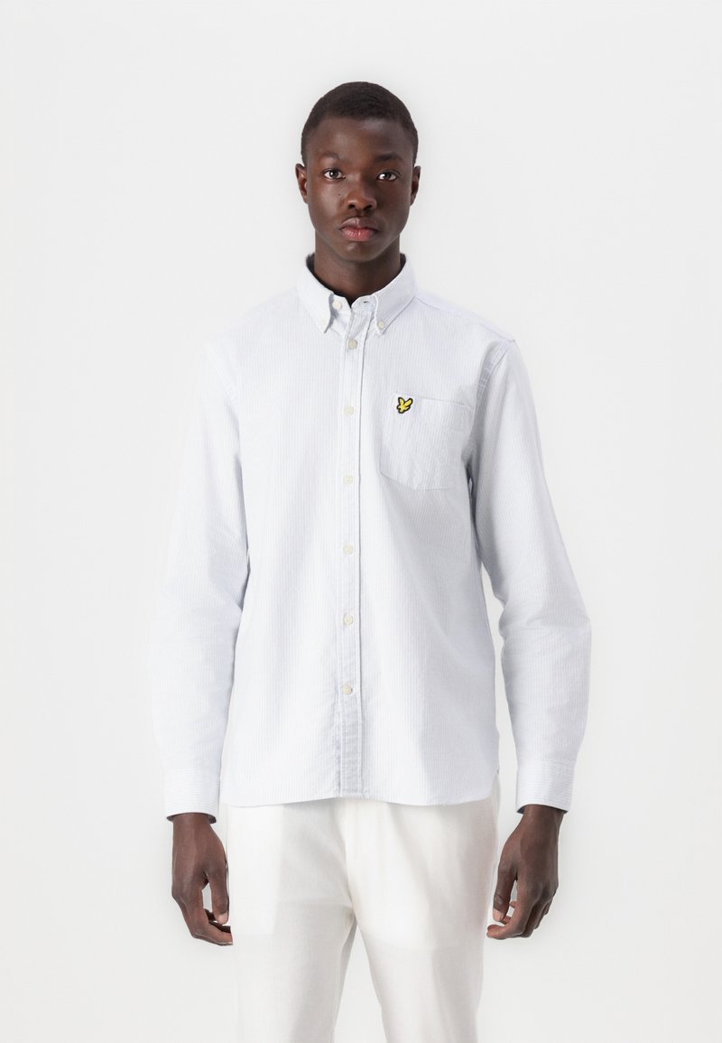 Cămașă button-up cu dungi albastre deschise, având un buzunar pe piept cu un logo galben. Manșete lungi, guler standard și țesătură ușoară.