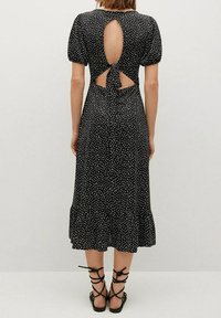 Czarna midi sukienka w białe kropki, z bufiastymi rękawami, wycięciem na plecach i kokardą. Miękka tkanina z opadającym, falbaniastym dołem.
