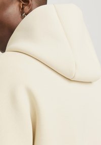 Crème-kleurige hoodie met een zachte textuur en een relaxed fit. Heeft een ronde capuchon en minimale stikseldetails.