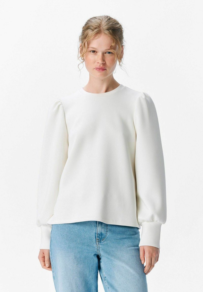 Weißer Pullover mit langen Ärmeln, runder Ausschnitt und puffigen Ärmeln, aus einem weichen Material gefertigt, kombiniert mit hellblauen Jeans.