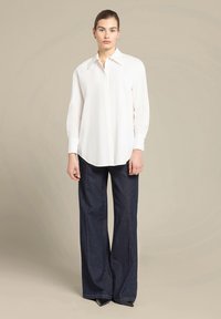 Witte button-up overhemd met een klassieke kraag, gecombineerd met donkerblauwe wijde jeans. Gladde stoftextuur, minimaal ontwerp en lange mouwen.