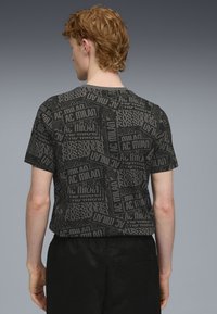 Sort T-shirt med et grafisk mønster over hele, indeholdende teksten "AC Milan" i forskellige stilarter. Kortærmet med rund hals.