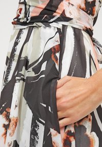 Robe avec un motif abstrait en noir, blanc, corail et beige. Fabriquée en tissu léger avec une coupe décontractée et des poches latérales.