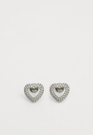 Des boucles d'oreilles en argent en forme de cœur présentent un centre creux entouré de petits strass, ajoutant une brillance texturée au design.