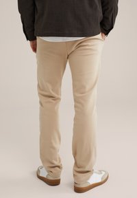 Bēša kokvilnas bikses ar šauru piegriezumu, apvienotas ar baltām un pelēkām sporta apaviem ar strukturētu zoli un auklām. Minimālistisks dizains.