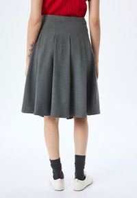Gonna plissettata grigia con tessuto testurizzato, di lunghezza media, con vita alta. Indossata con calze grigie e scarpe bianche per un look casual.