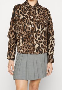 Leopard print jacket in brown and black, with two chest pockets, silver buttons, and a relaxed fit. Worn over a pleated gray skirt.