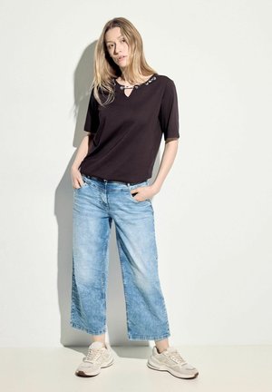 Top negro de manga corta con escote redondo y detalles metálicos, combinado con pantalones vaqueros de pierna ancha de color azul claro y zapatillas beige.