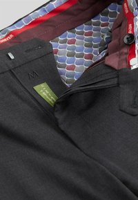 Pantaloni neri con una tasca con cerniera e un'etichetta verde. All'interno hanno una fodera a fantasia con accenti rossi e blu.