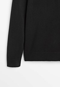 Manche et bas du torse d'un pull en maille noire avec poignets et ourlet côtelés sur fond blanc.