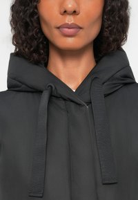 Zwarte hooded jacket met trekkoorden, gemaakt van gladde stof, met een lichtglanzende textuur en een eenvoudig, minimalistisch ontwerp.
