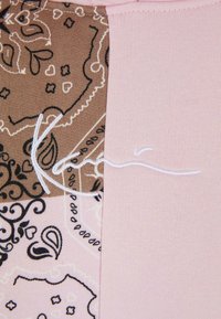 Tekstil med delt design: den ene siden har et brunt mønstrete stoff, mens den andre siden er i en ensfarget lys rosa. Hvite søm detaljer er til stede.