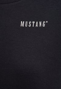 Czarny bawełniany t-shirt z białym logo "MUSTANG" umieszczonym na środku klatki piersiowej, o drobnej, gładkiej fakturze.
