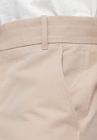 Beige auduma bikses ar gludu tekstūru, ar plakanu jostu, sānu kabatām un redzamām šuvju detaļām.