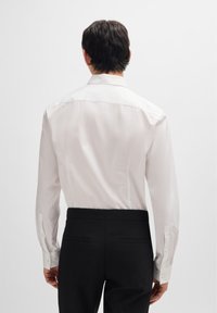 Biała koszula z długim rękawem, ze standardowym kołnierzykiem, gładką teksturą i mankietami na guziki, w połączeniu z czarnymi spodniami z tylnymi kieszeniami.