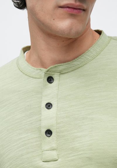 Šviesiai žalia Henley tipo marškinėlių su tekstūruotu paviršiumi, apvaliu iškirpimu, trimis juodais mygtukais ir subtiliu margintumu.